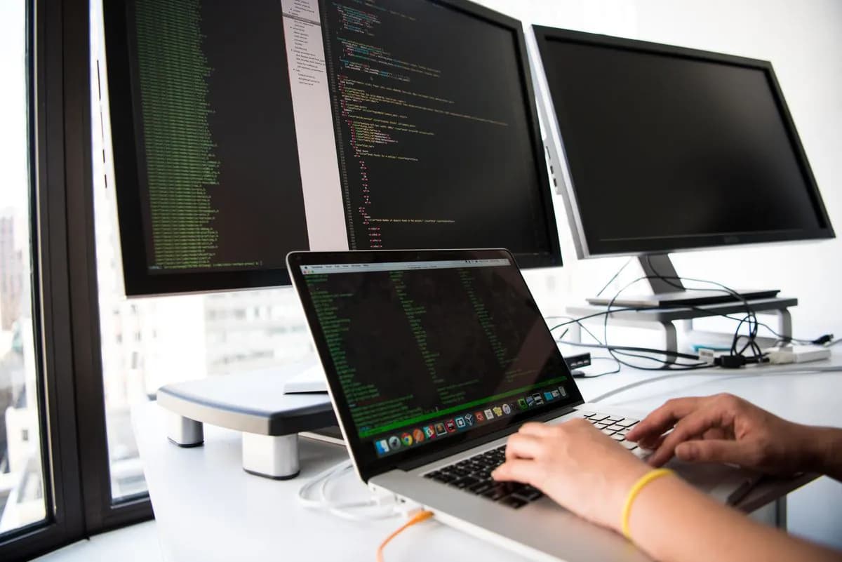 Programuotojas rašo kodą prie kelių monitorių