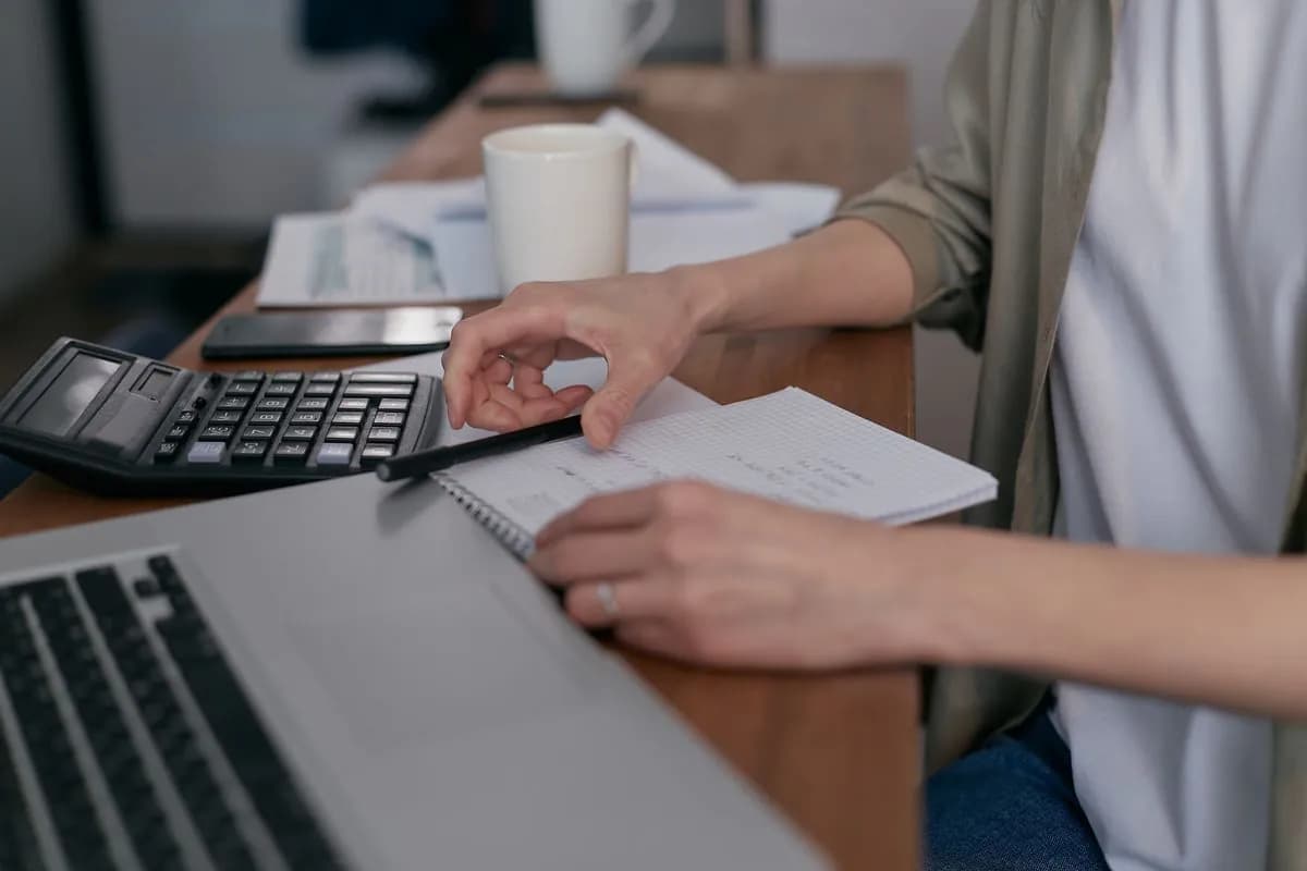 Alguém calcula faturas num portátil, com uma calculadora ao lado