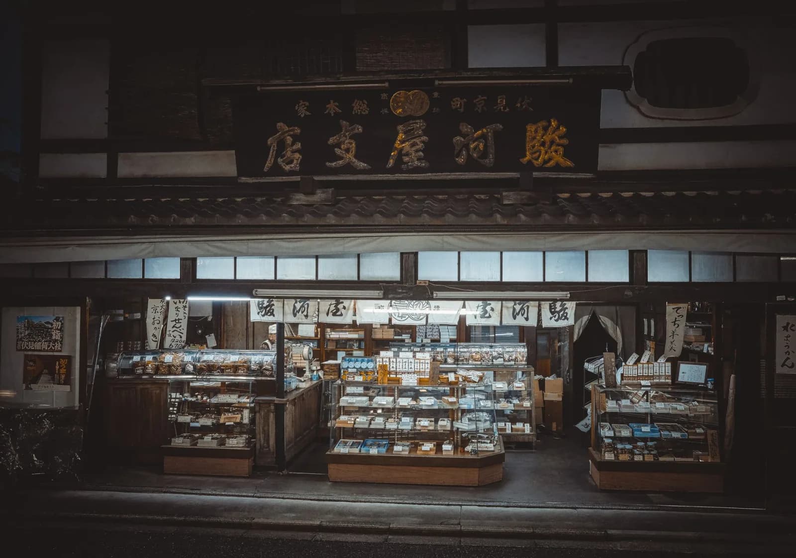 Charming illuminated traditional storefront in Kyoto, offering an array of goods under Japanese signage.