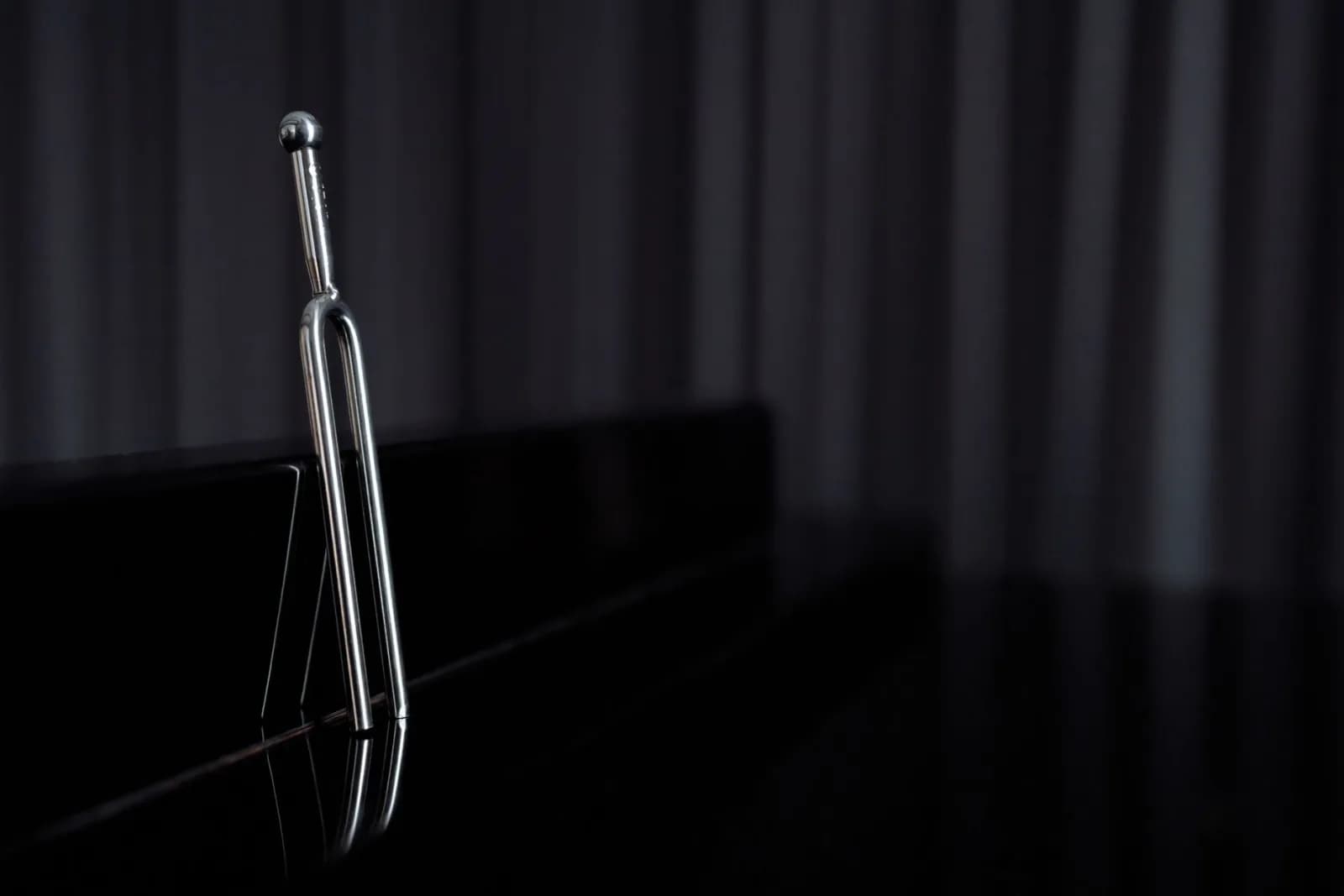 A close-up of a metal tuning fork standing on a reflective piano surface with dark background.
