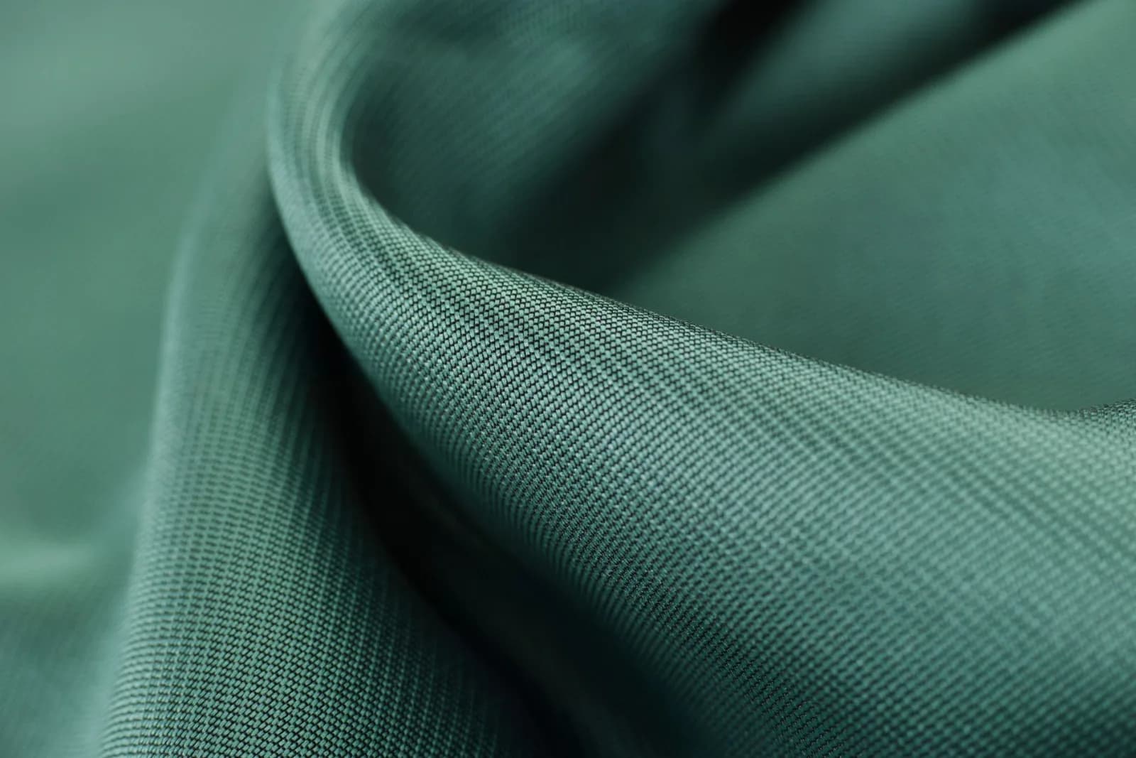 Close-up texture shot of elegant green satin fabric highlighting its smooth and soft surface.