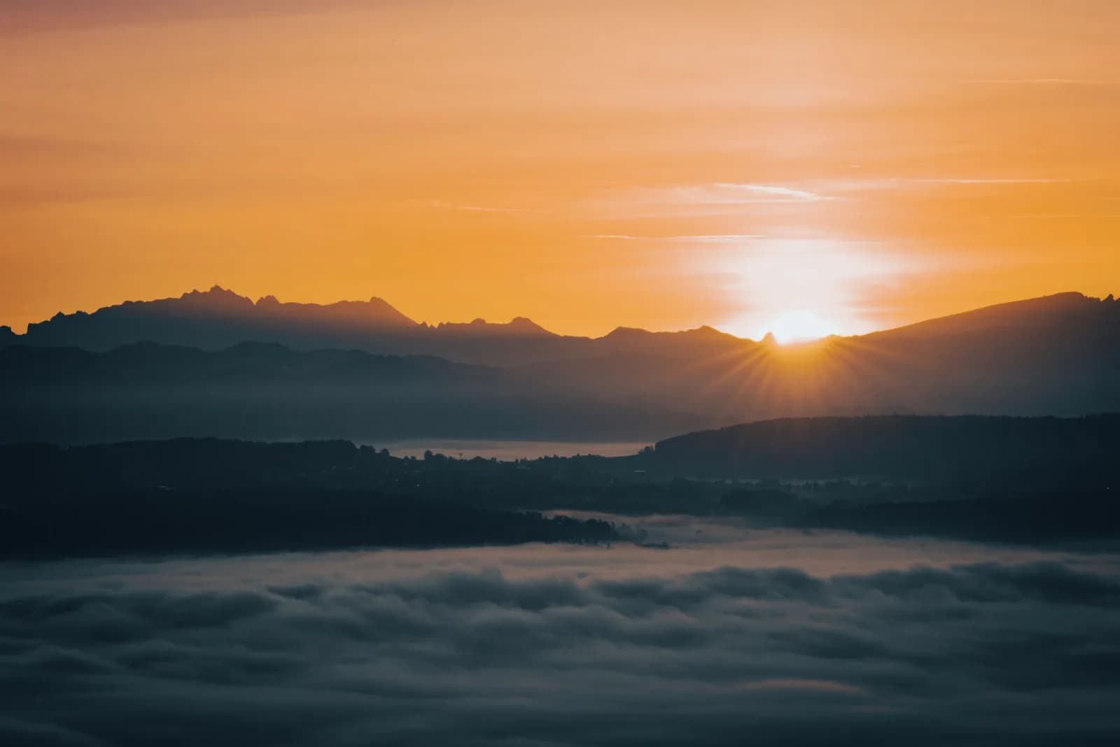 A stunning sunrise over a mountainous landscape with clouds, creating a dramatic and serene scene.