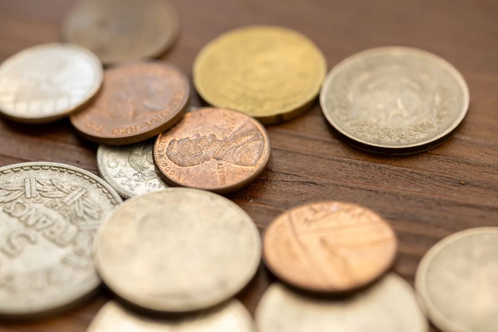 A detailed close-up image showing various vintage coins scattered on a wooden surface, capturing their unique textures and engravings.