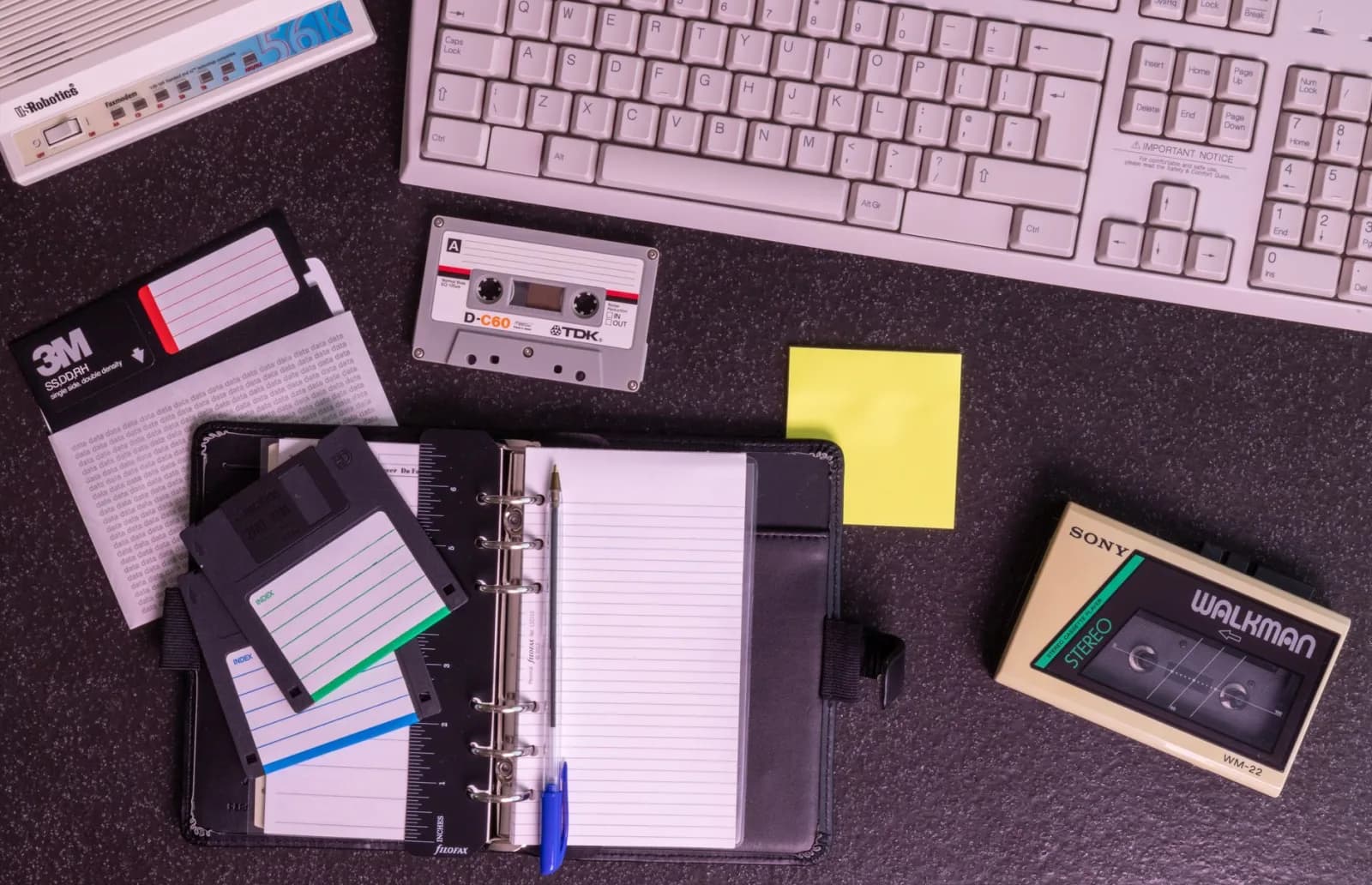 A nostalgic setup with vintage electronics like a Walkman, floppy disks, and a typewriter keyboard.