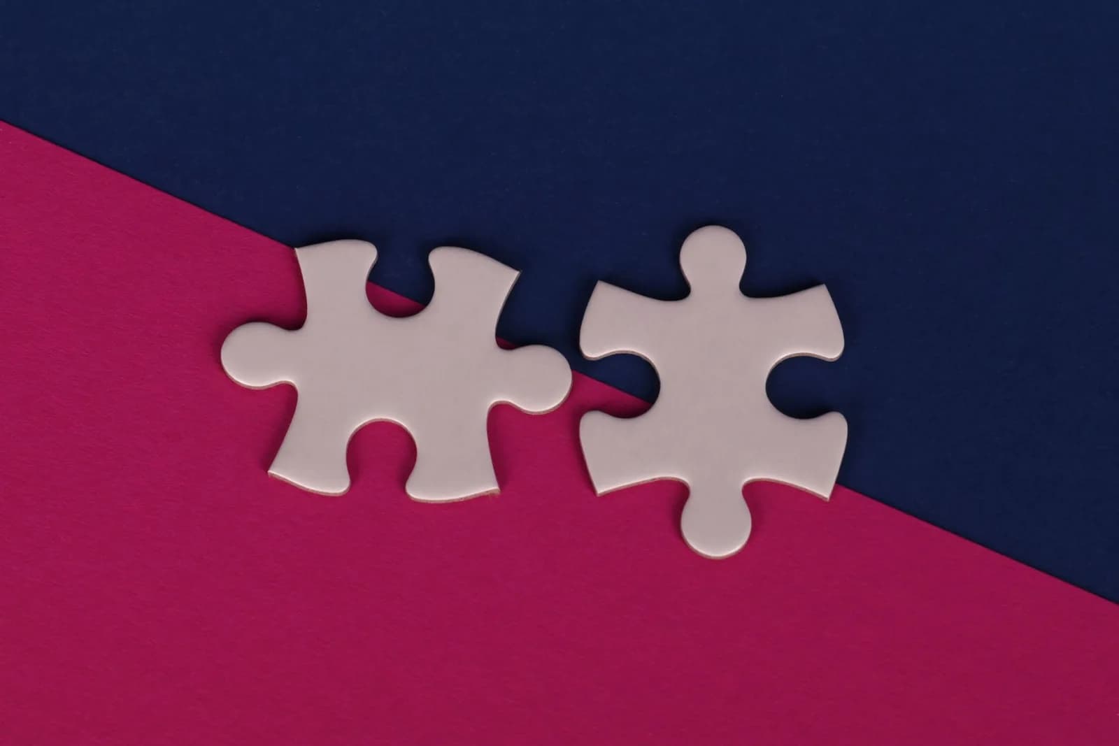 Close-up of white puzzle pieces on bold pink and navy background.