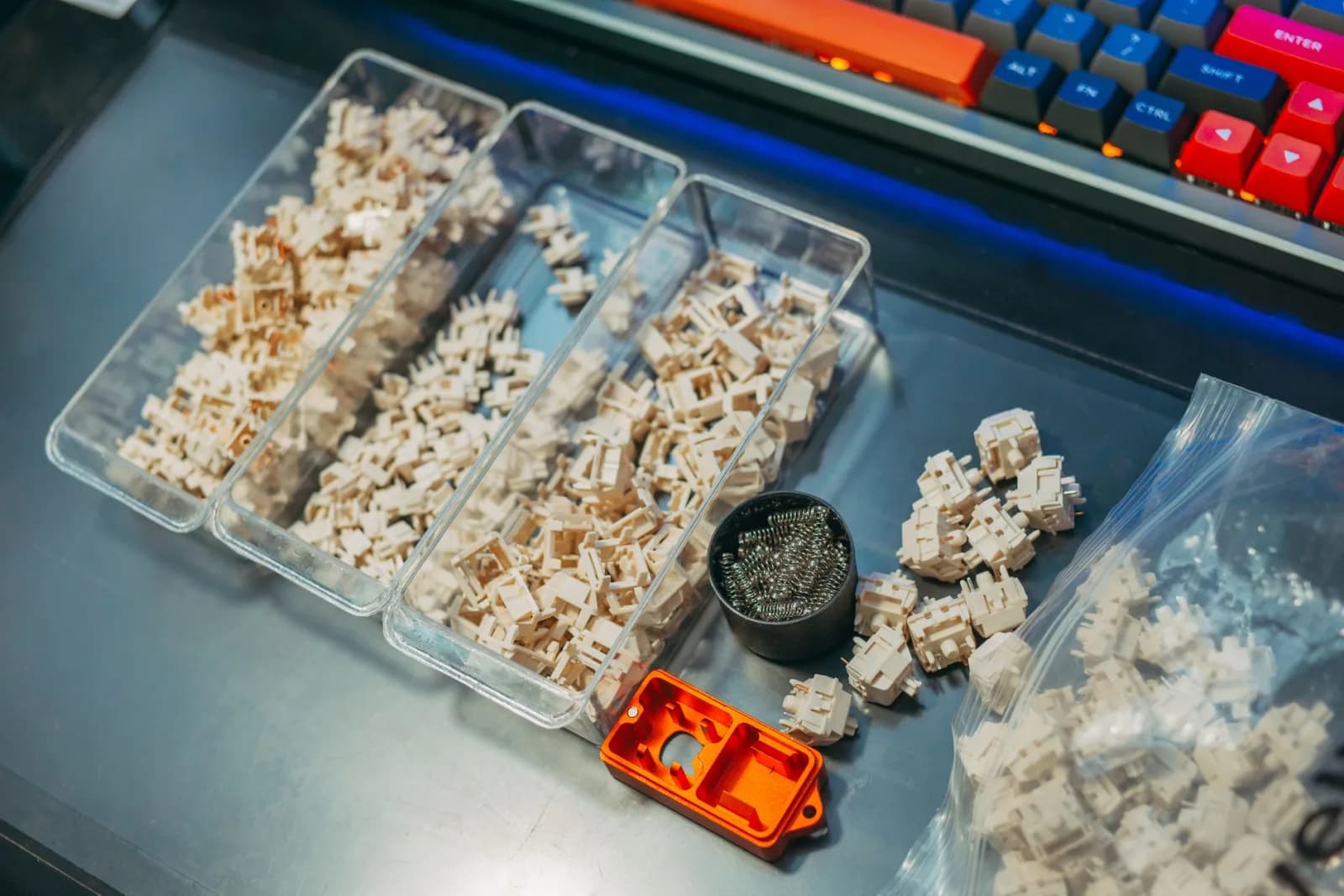 Close-up of mechanical keyboard switches and springs organized in containers on a desk setup.