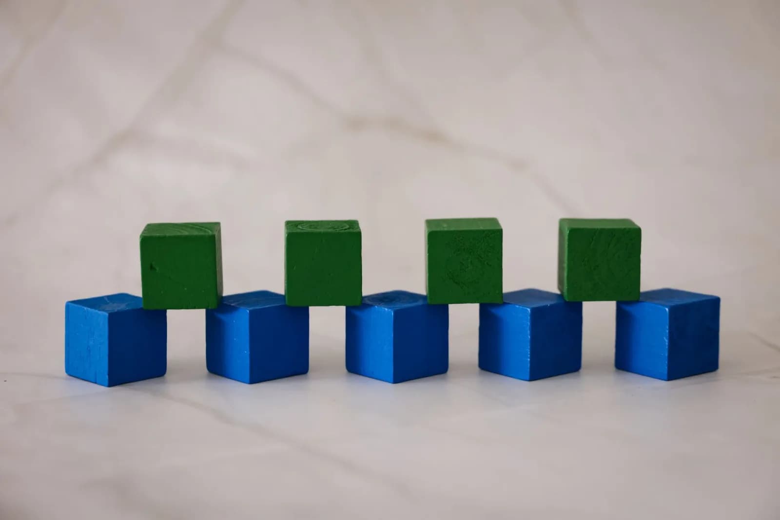 Arrangement of blue and green wooden blocks on a marble surface, creating a playful geometric pattern.