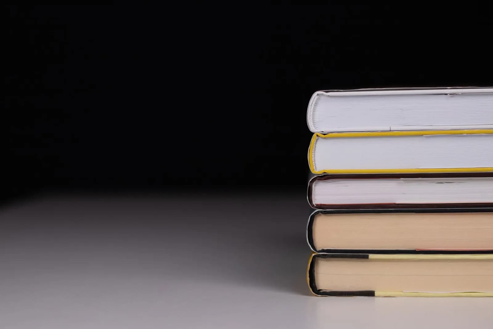 Minimalist stack of hardcover books with a black background and subtle lighting.