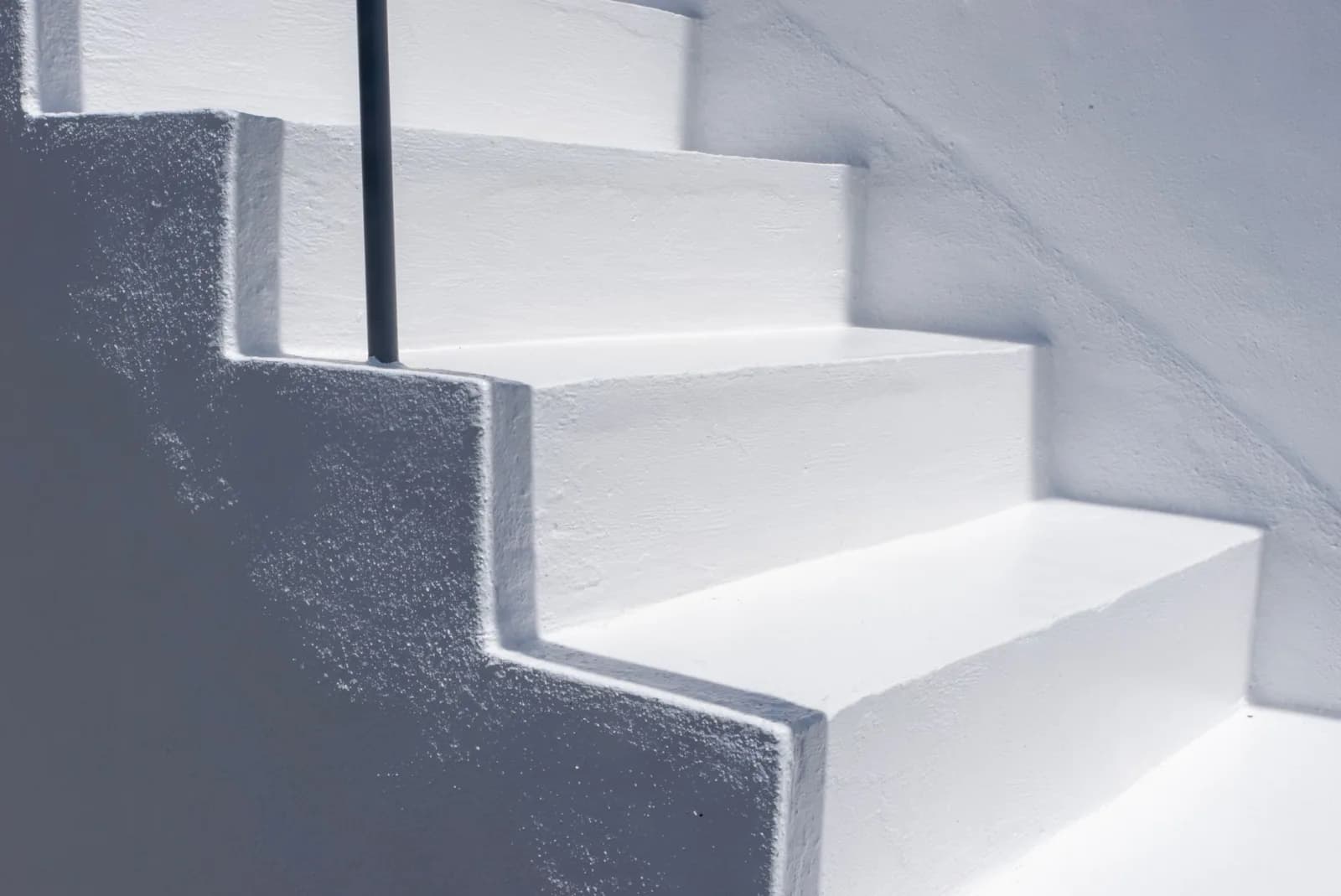 Close-up of a sunlit white staircase with a railing, showcasing minimalist architecture.