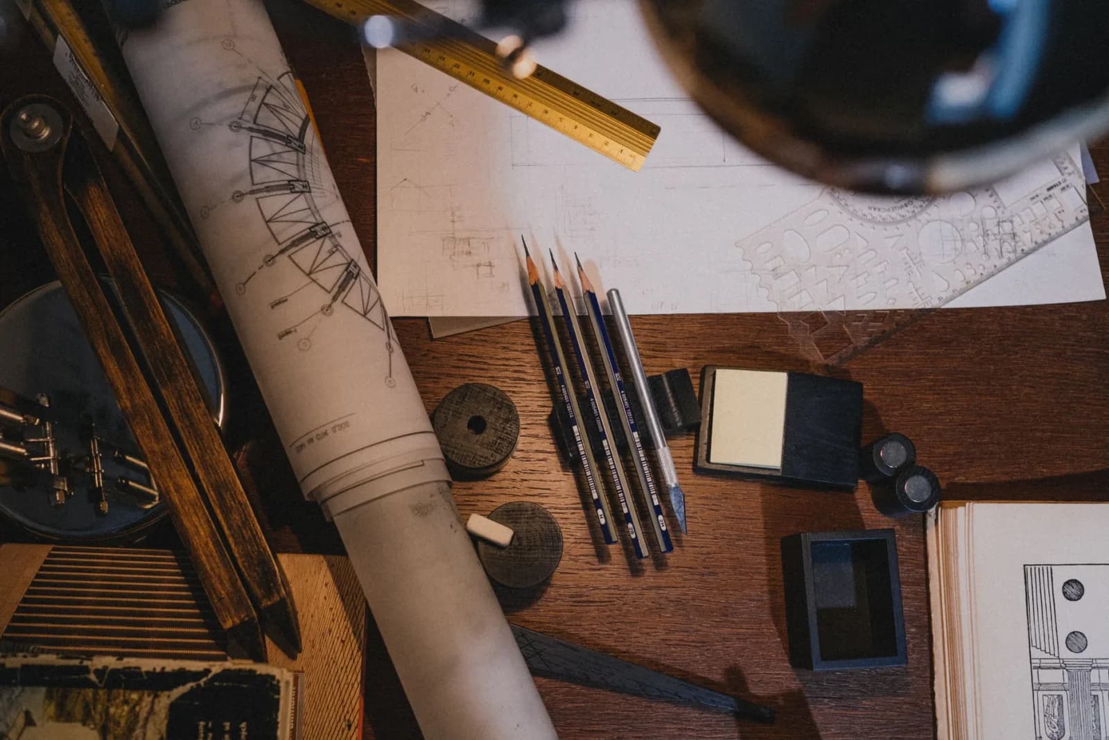 A cluttered workspace with architectural tools, blueprints, and pencils for design work.