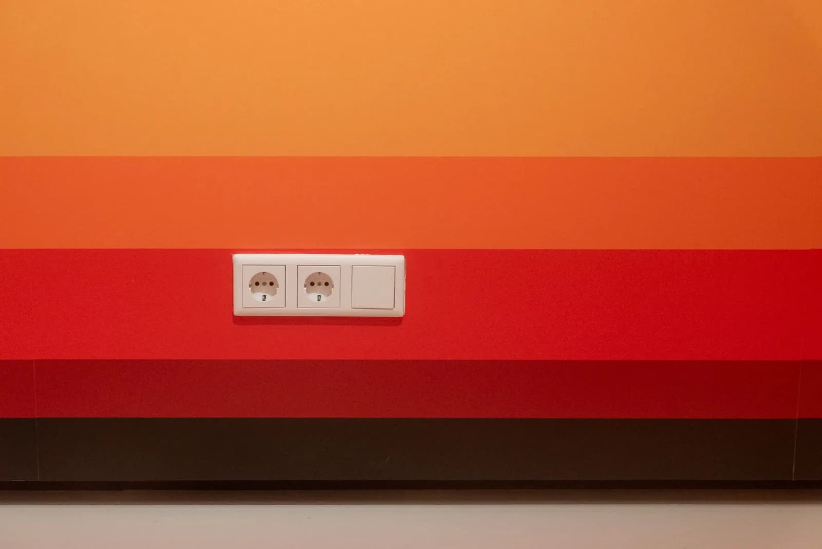 Minimalist design of orange and red striped wall with dual sockets.