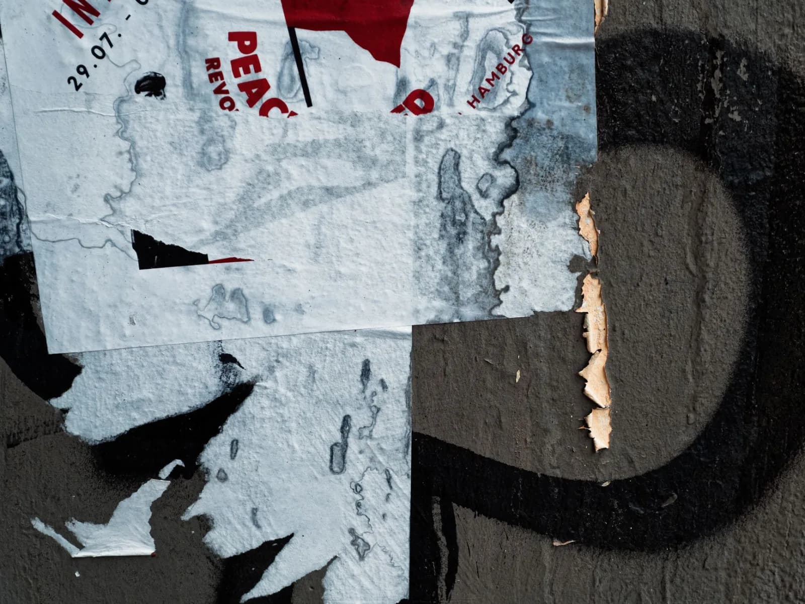 Close-up of layered torn posters peeling from a textured urban wall, showcasing street art decay.