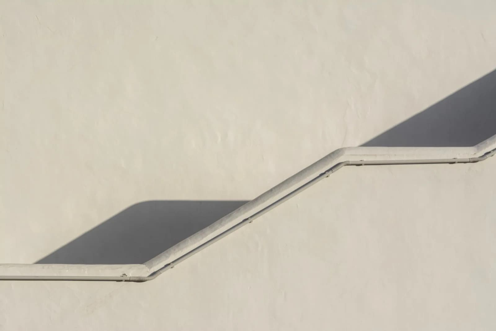 Elegant minimalist stucco wall with stairs casting geometric shadows, emphasizing simplicity.