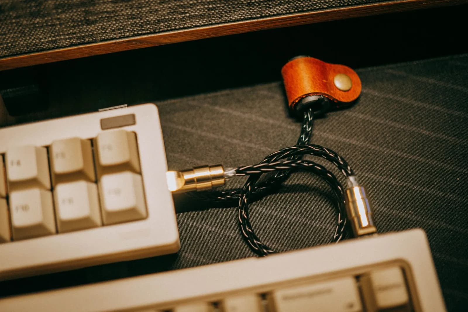 Close-up of a vintage mechanical keyboard with a braided coiled USB cable and leather strap.