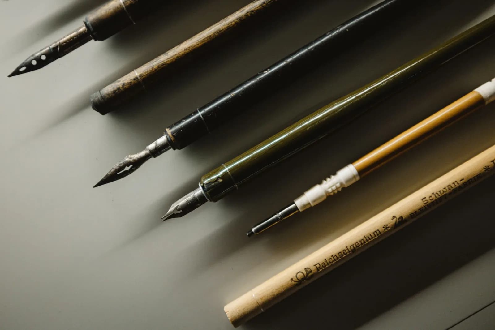 Close-up of vintage fountain pens and calligraphy nibs on a desk, showcasing writing tools.