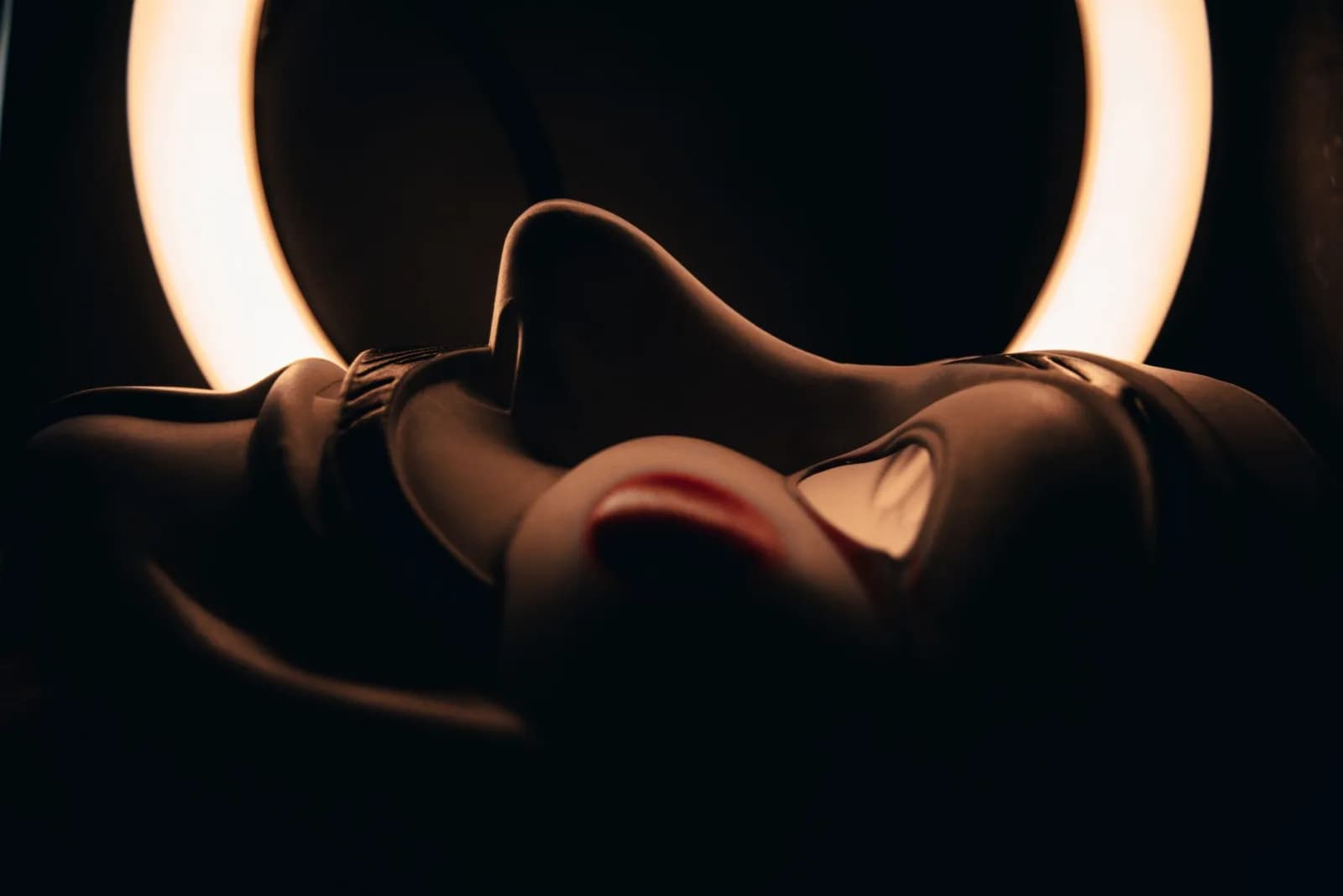A mysterious mask illuminated by a ring light in a dark setting, casting intriguing shadows.