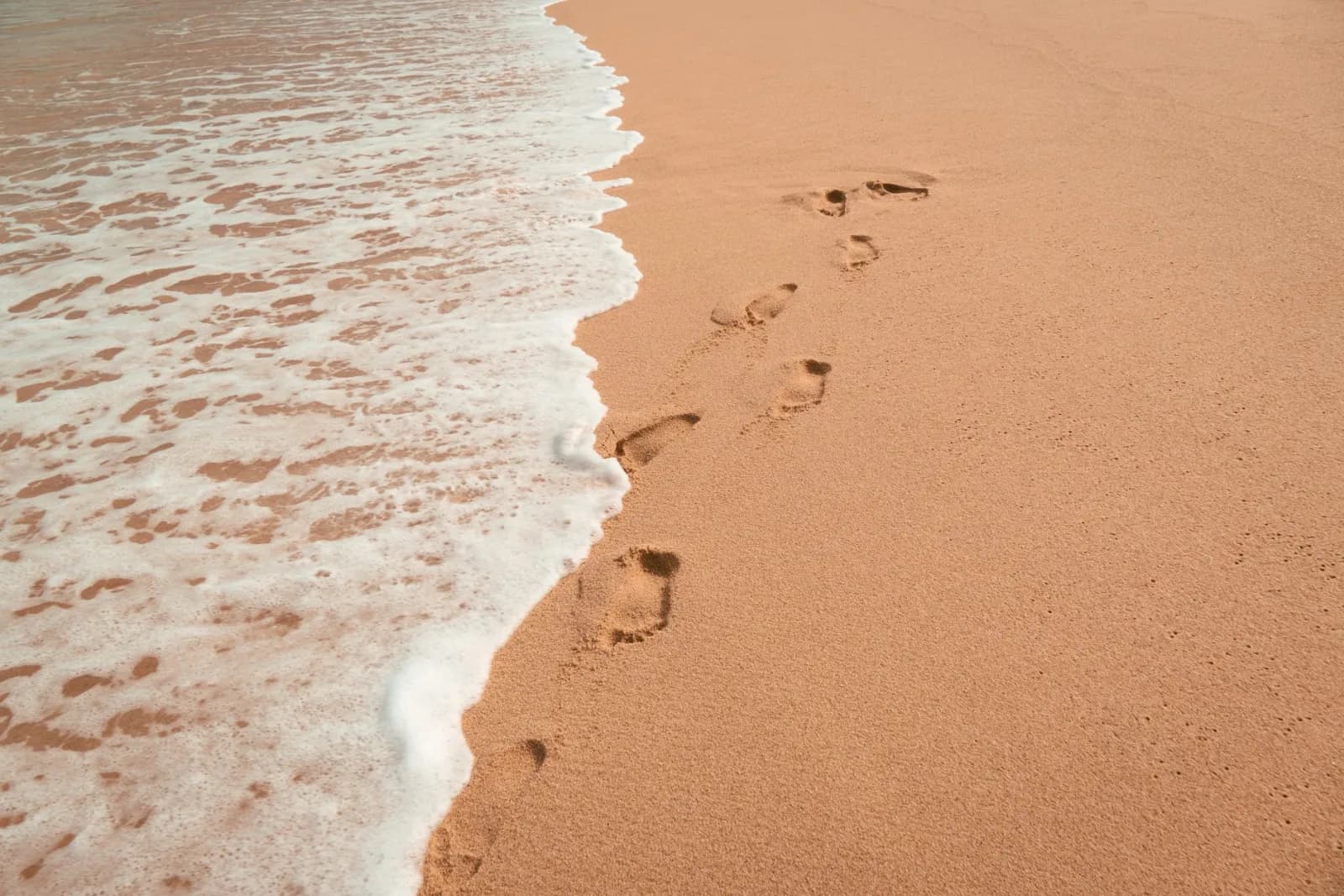 Footprints on sandy beach with ocean waves at daytime. Tranquil and serene ocean moment.
