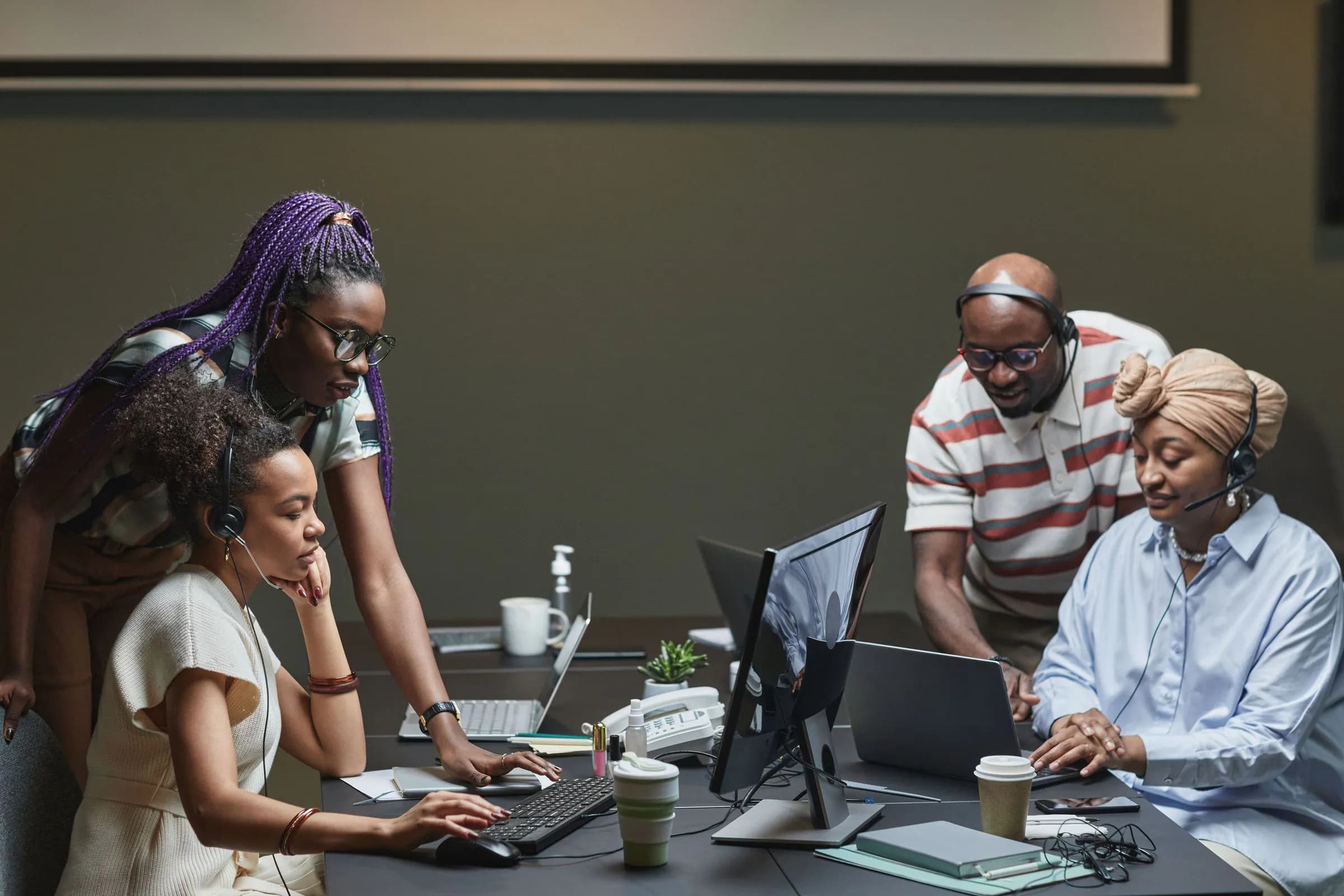 A team gathered around a colleague's screen in a small office
