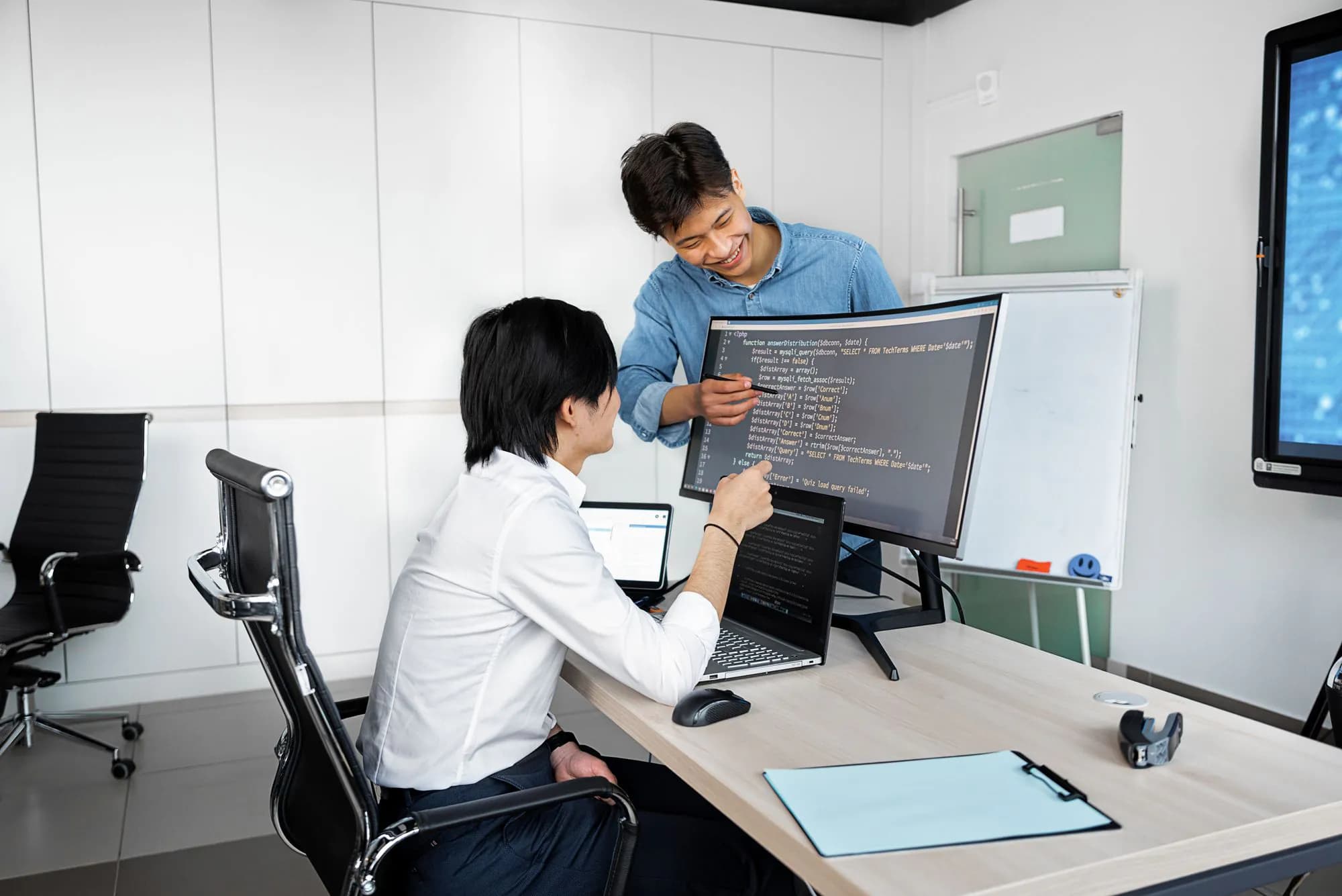 Two engineers working together at a desk with laptops and monitors