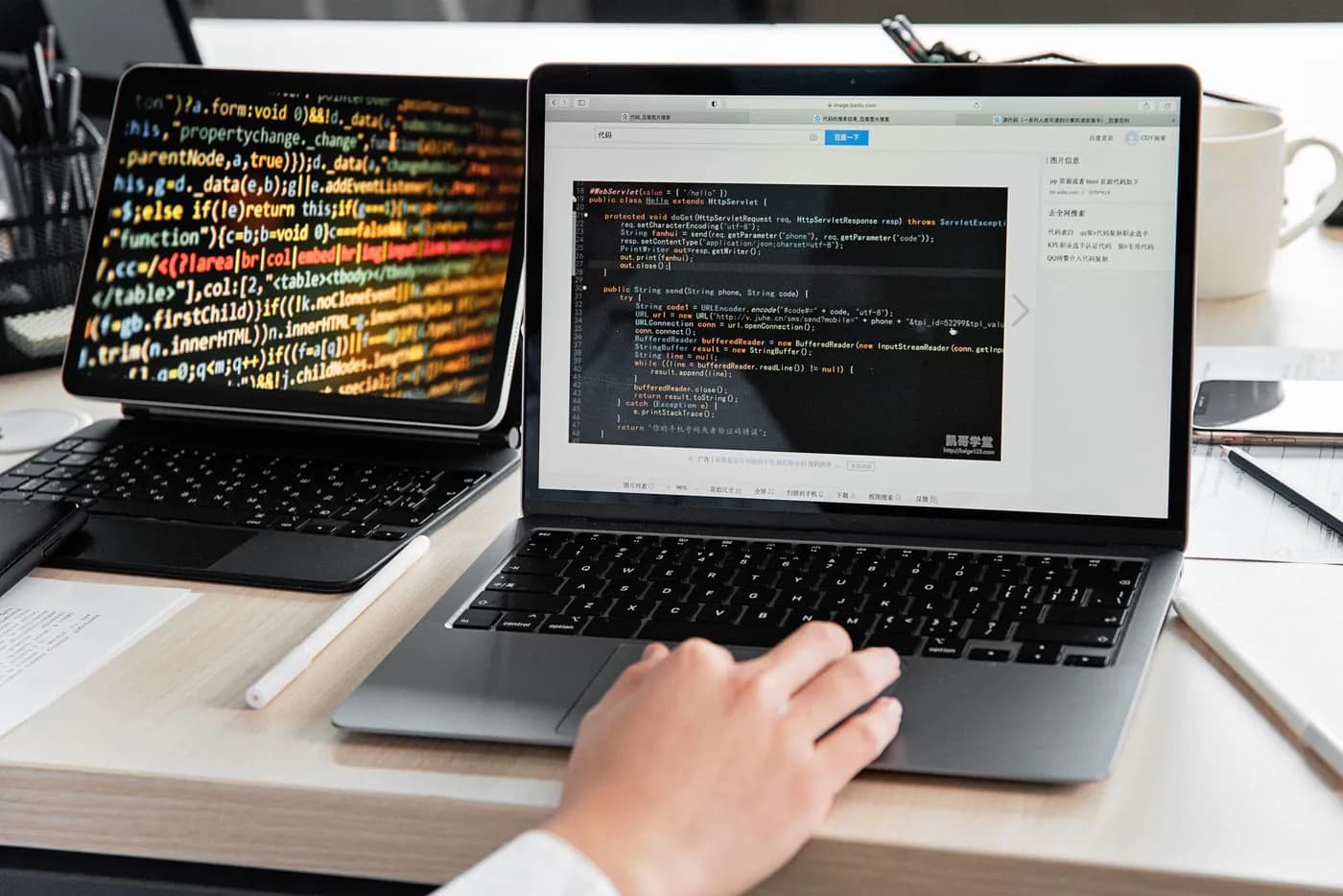 A developer writing code on a laptop beside a second screen