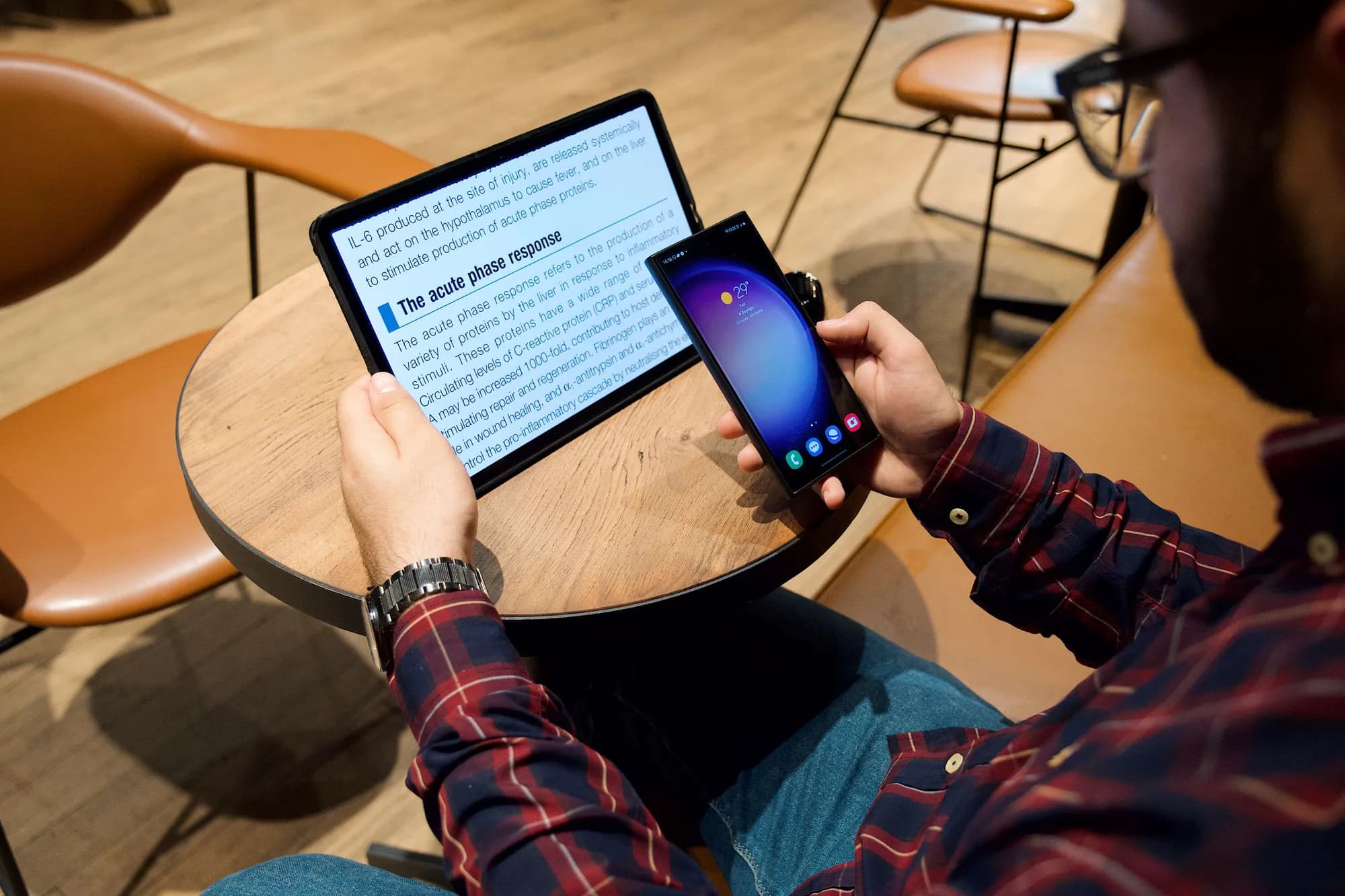 A man reading on a tablet and a phone at a cafe table