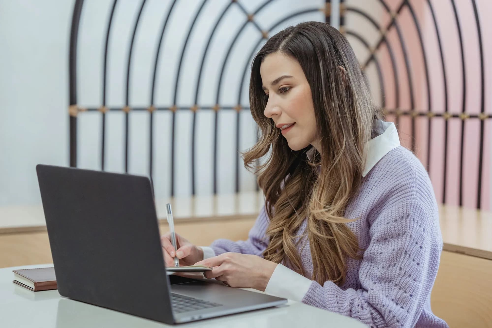 A woman writing notes in a planner beside her laptop