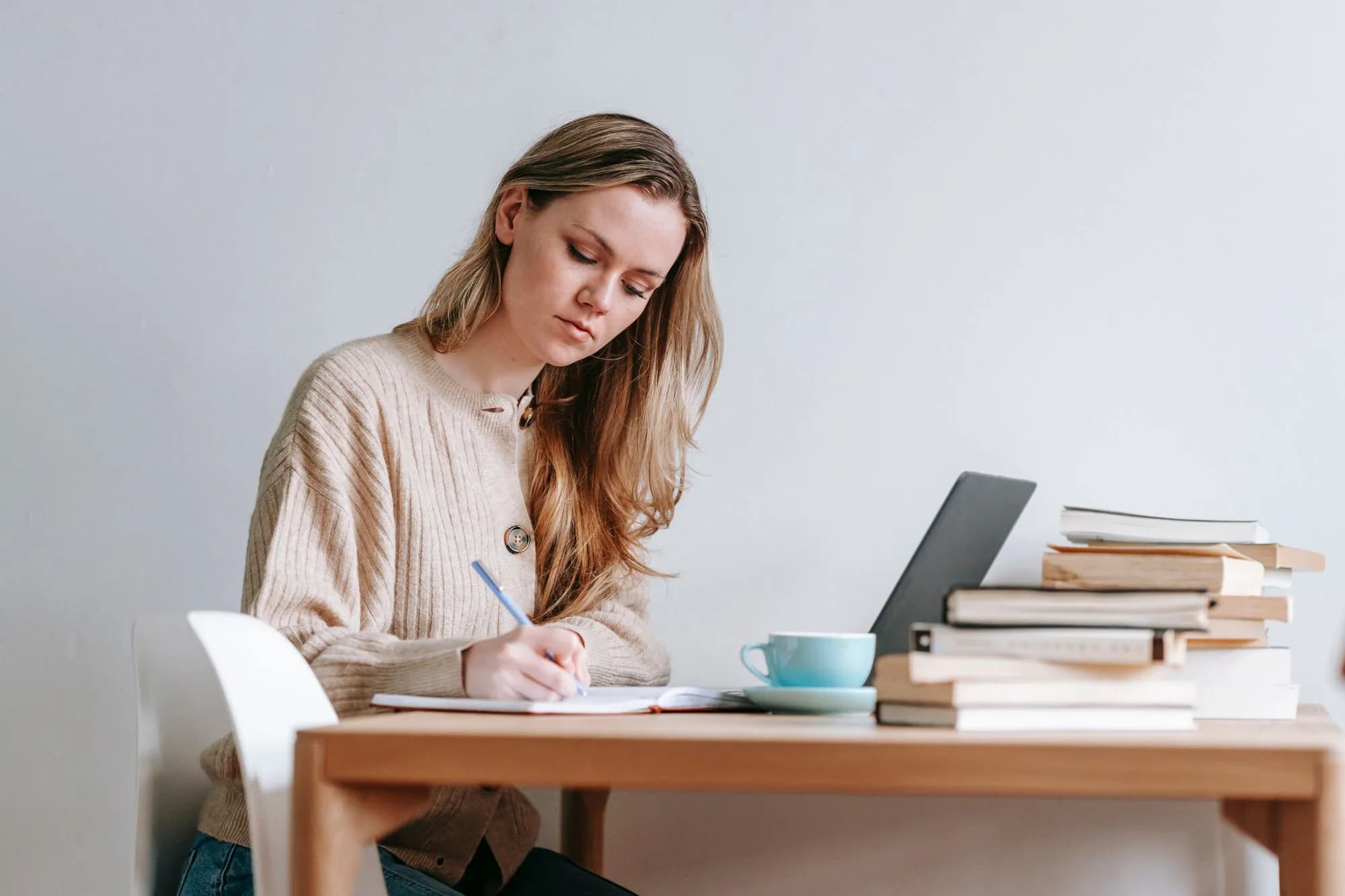A woman taking notes beside a pile of books and a cup of coffee