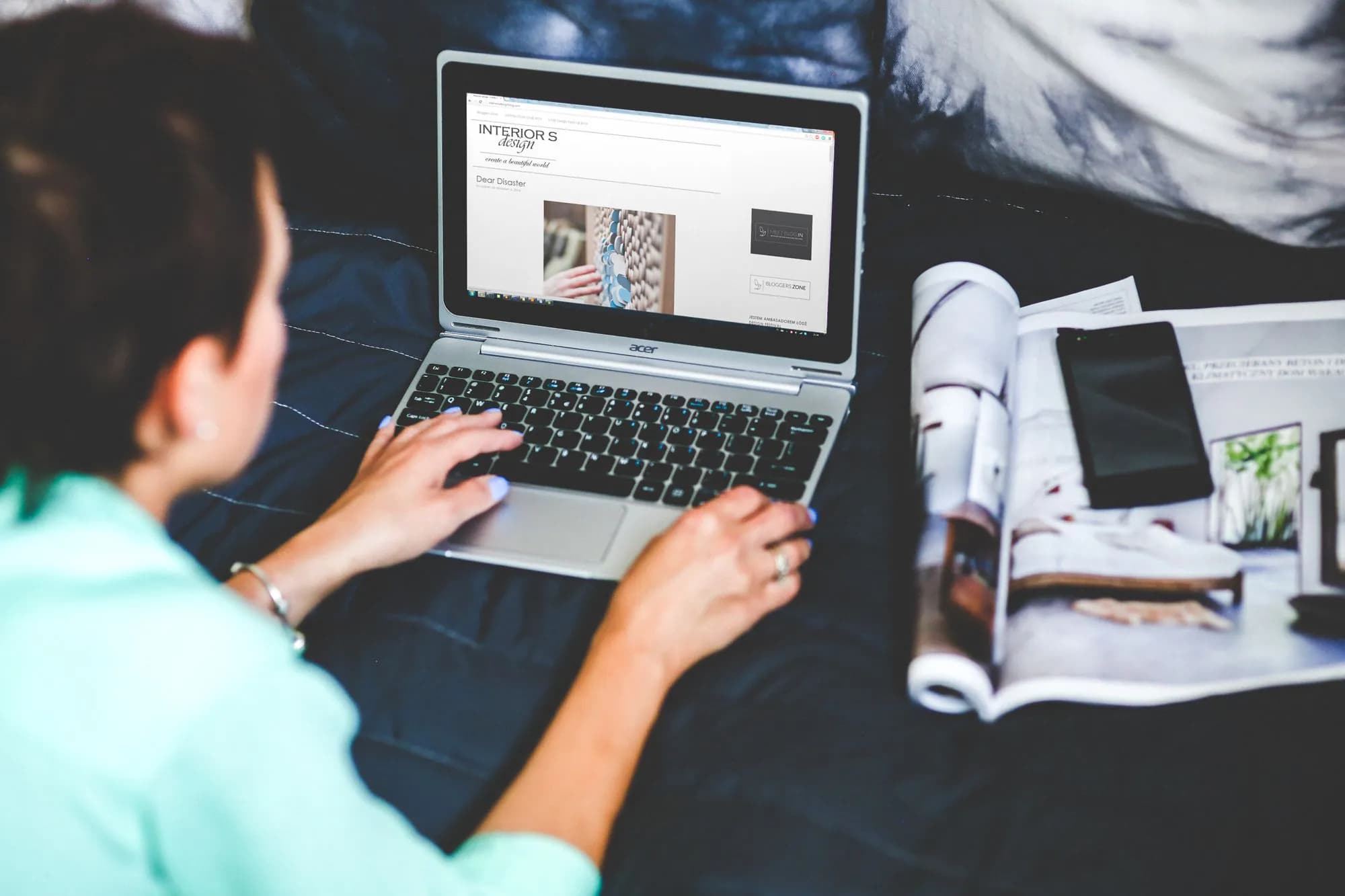 A woman blogging on a laptop with a magazine beside her