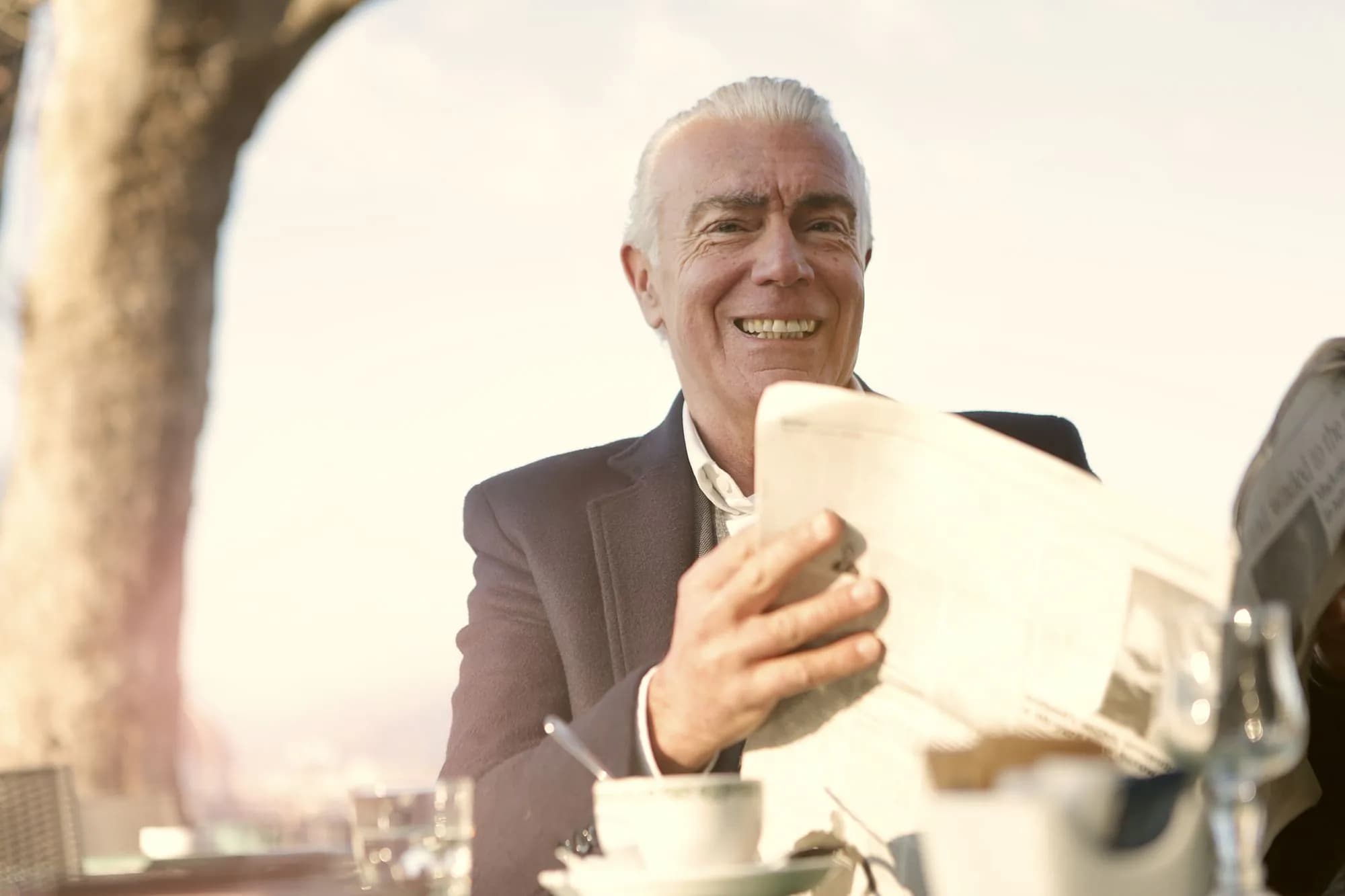 A smiling older man outdoors with coffee and his phone