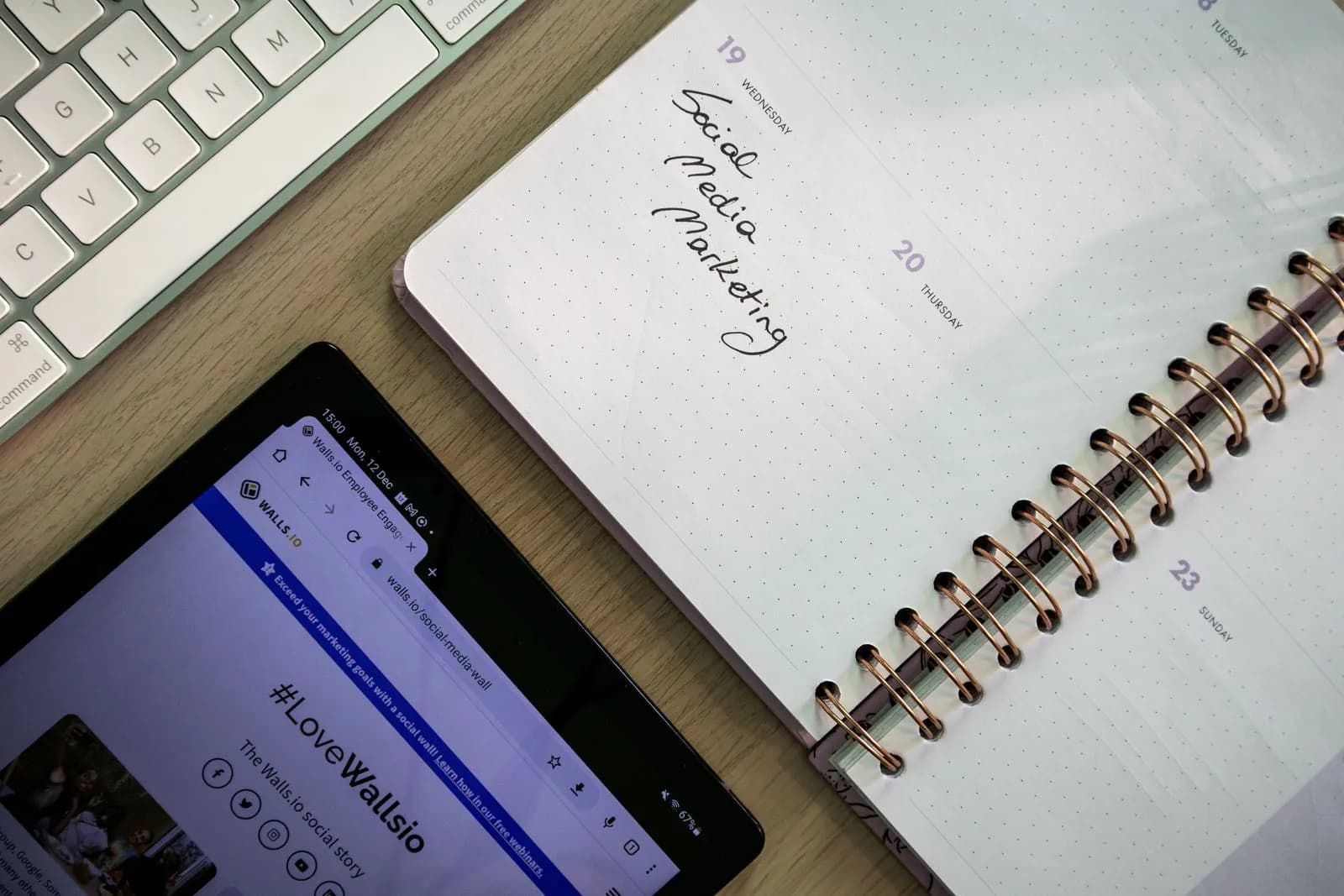 A notebook, a tablet and a keyboard laid out to plan social media posts