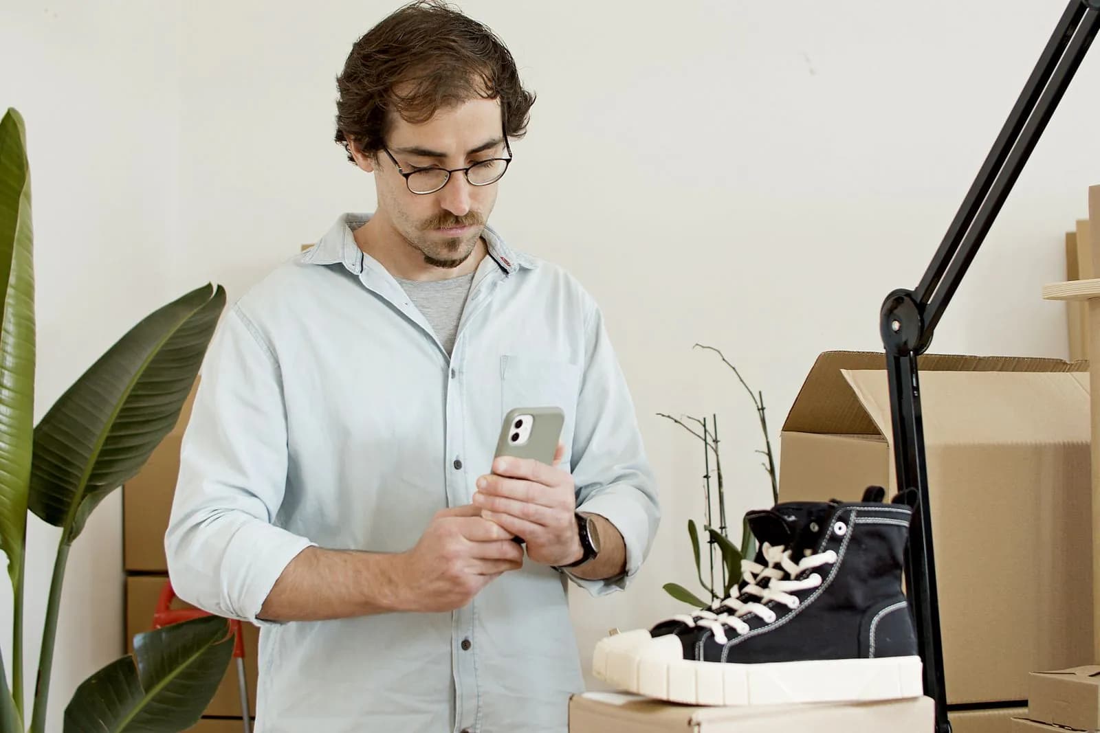 A man photographing a pair of sneakers with his phone among shipping boxes