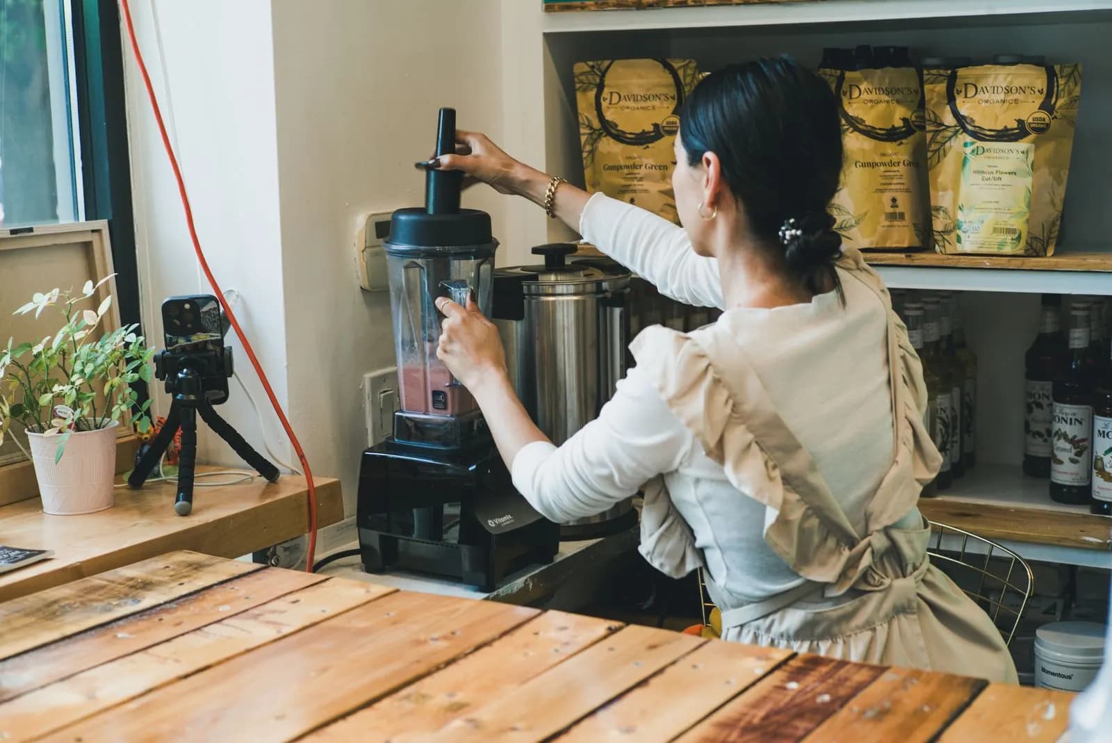 A woman making a smoothie in a cafe with a camera set up beside her