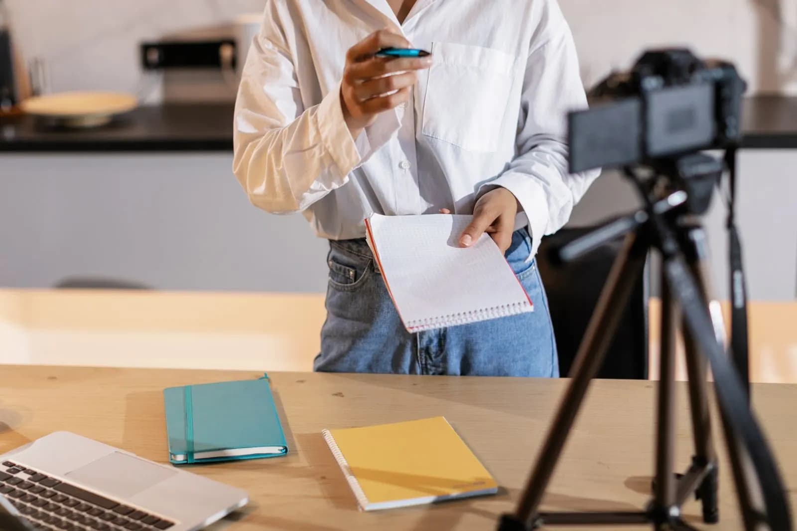 A woman with a camera, a laptop and notes planning a video