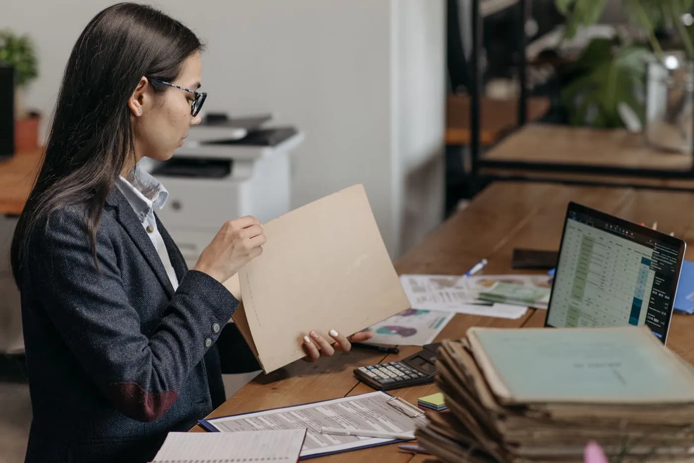 An auditor reviewing documents at her desk beside a laptop