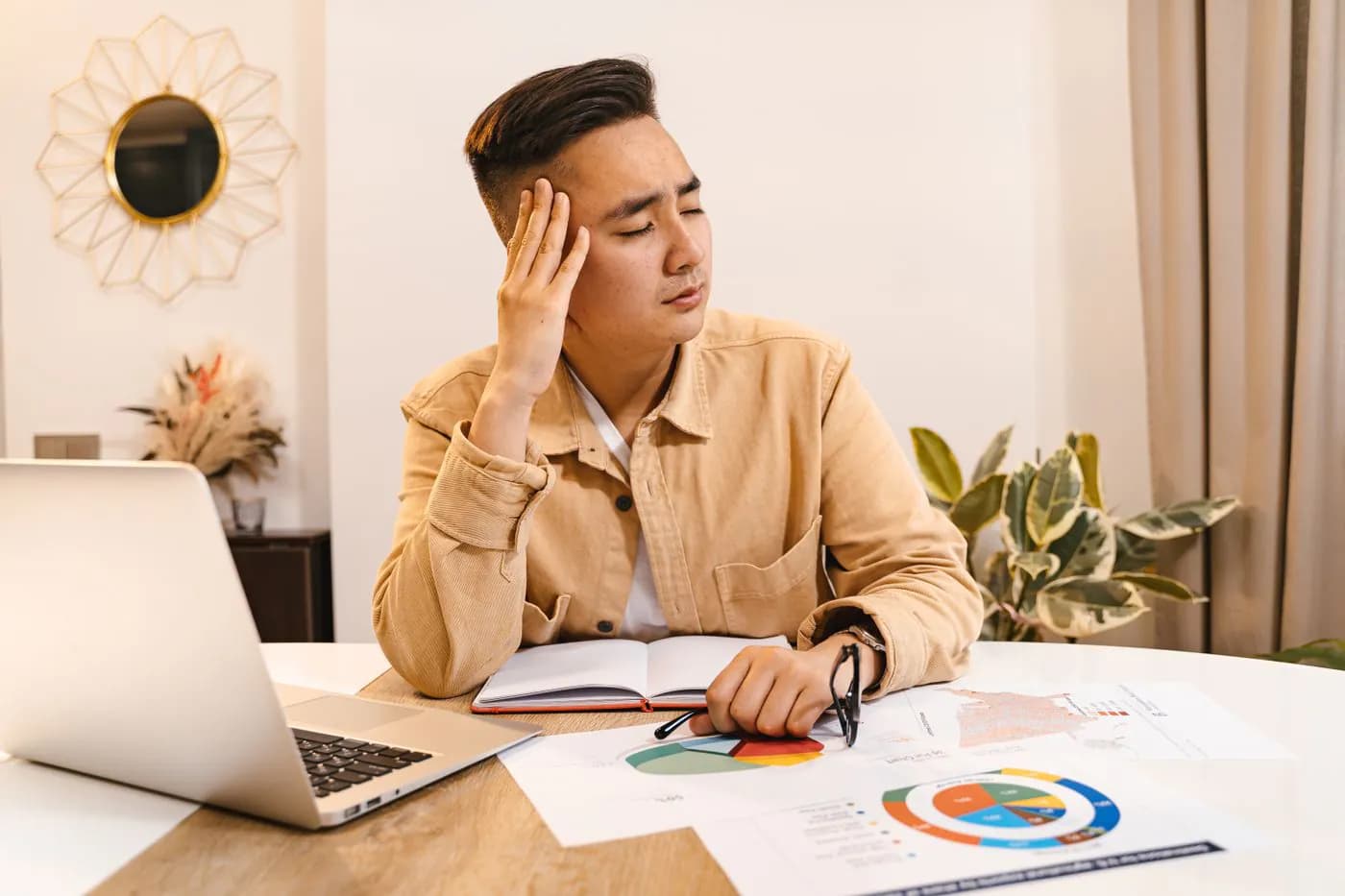 A business owner holding his head among invoices and a laptop
