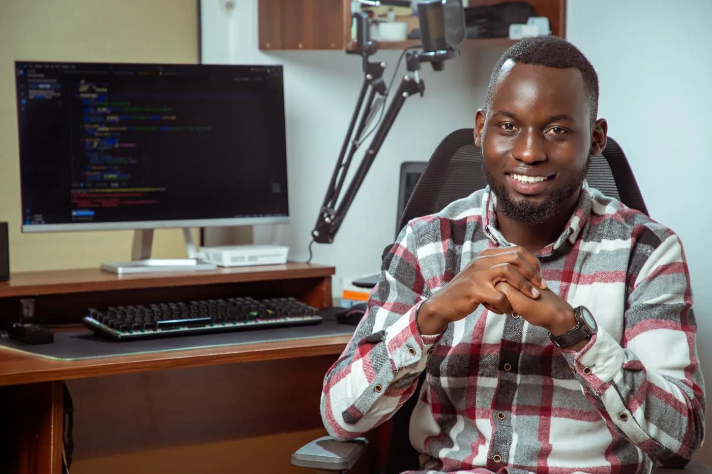 A smiling engineer at his desk, his screens behind him