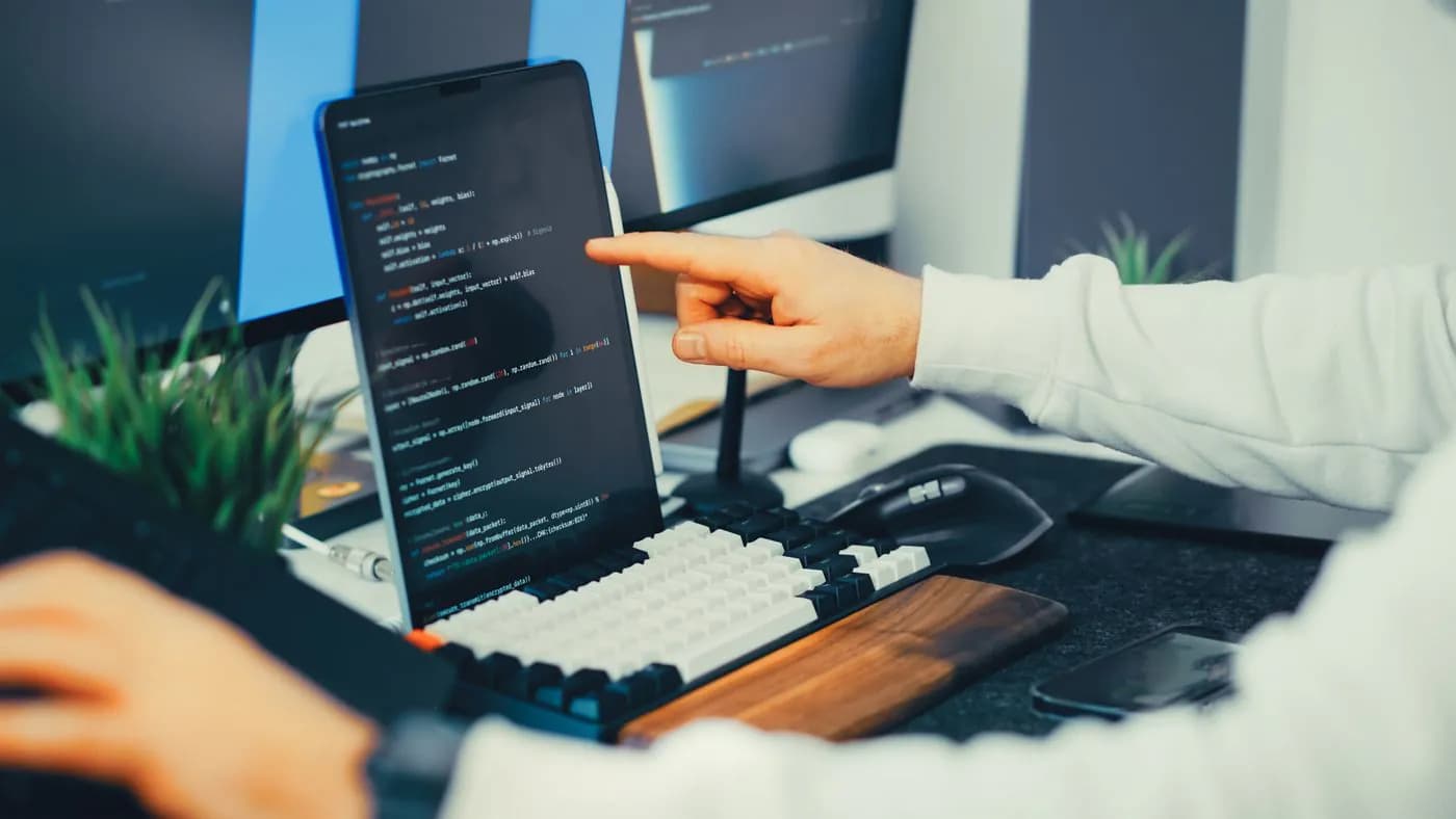 An engineer reviewing code on a laptop and a monitor