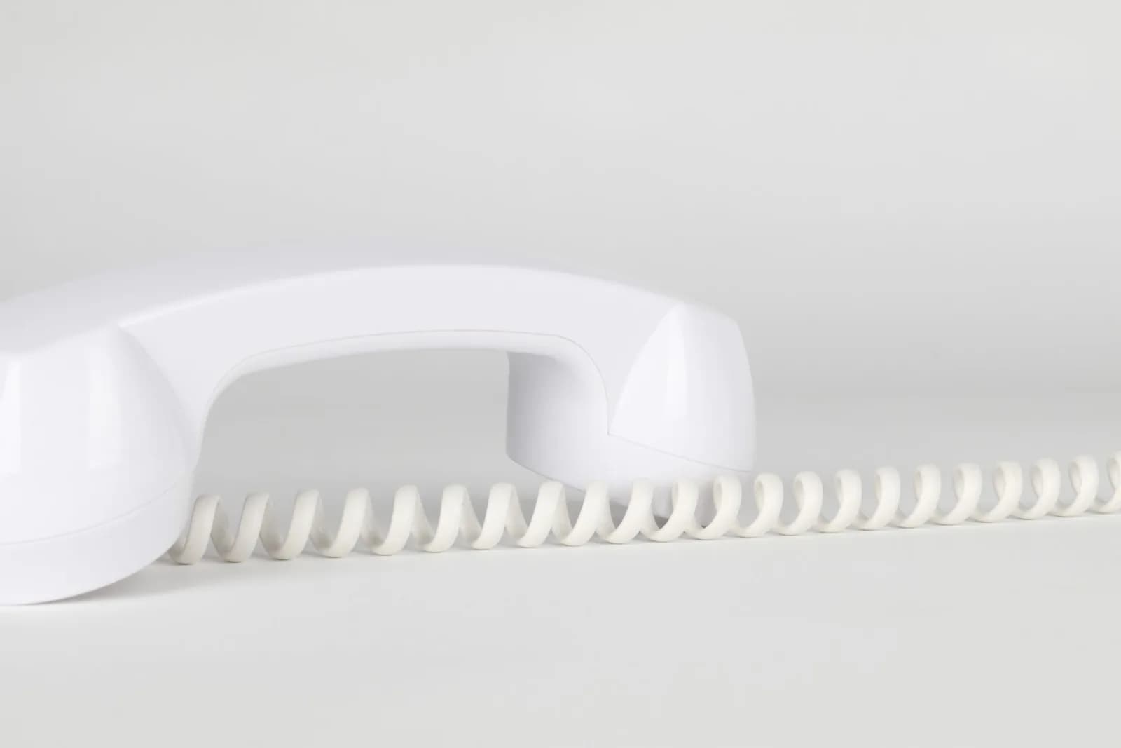 Close-up of a white telephone handset with coiled cord on a neutral background.