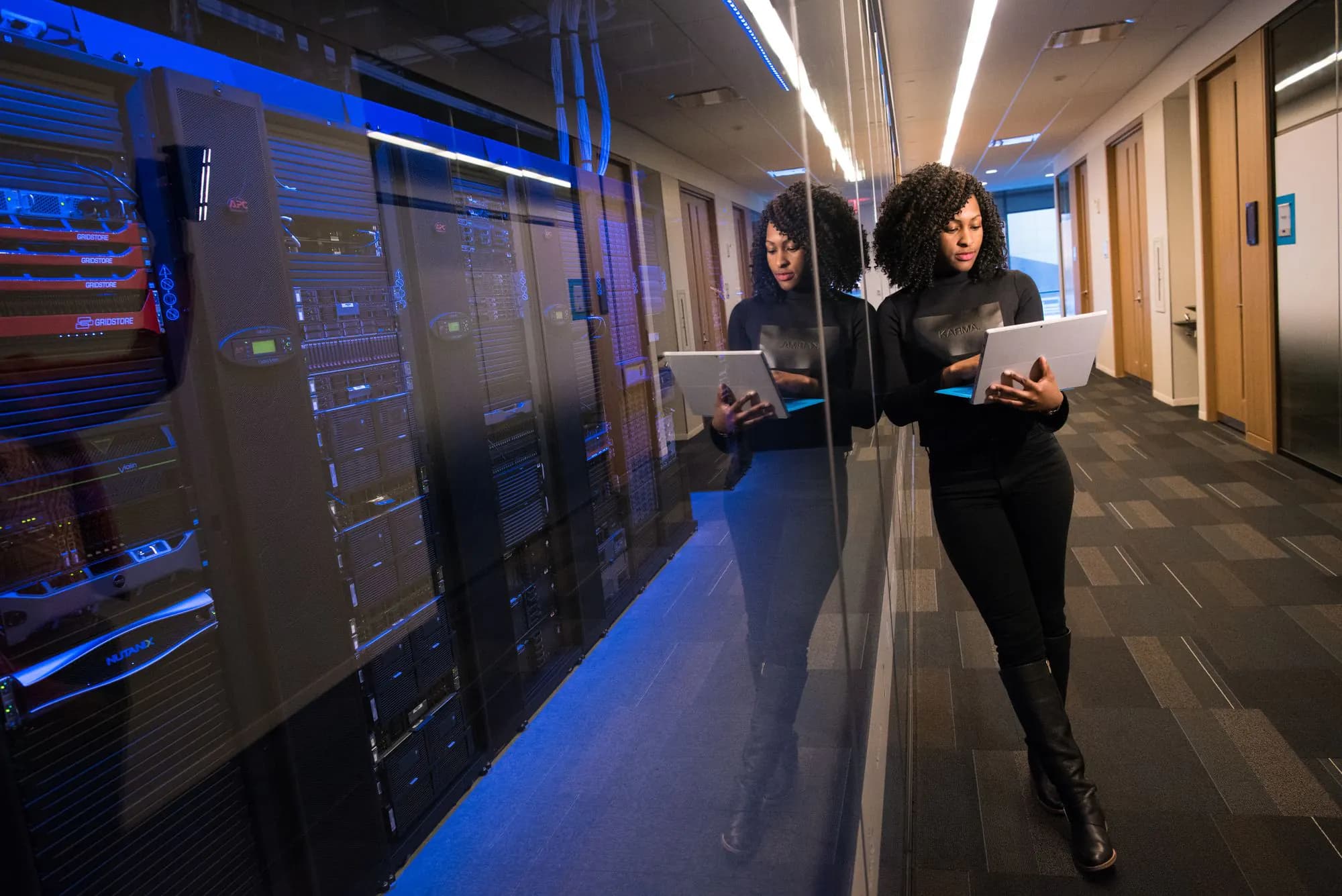 An engineer with a laptop walking along server racks in a data centre.