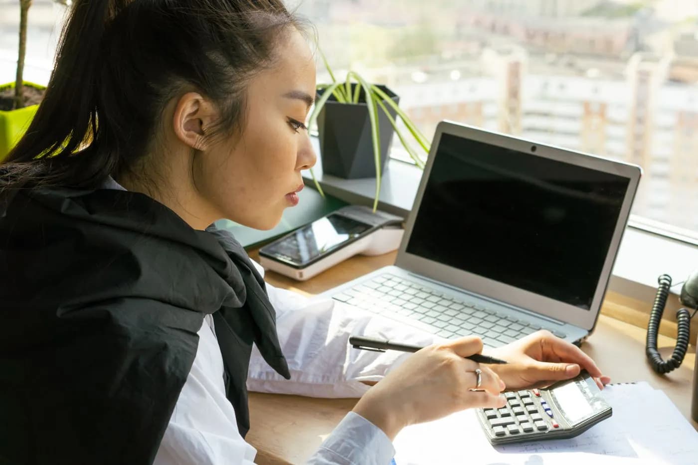 A woman working through invoices with a calculator and a laptop