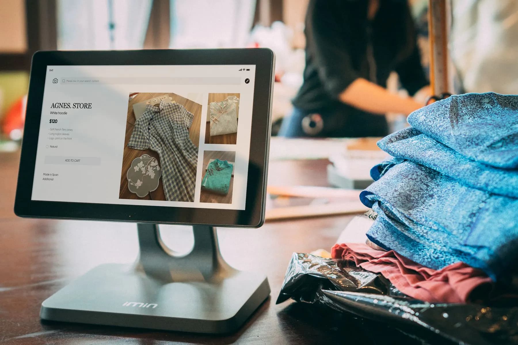 A boutique's product pages shown on a tablet beside the clothes they sell