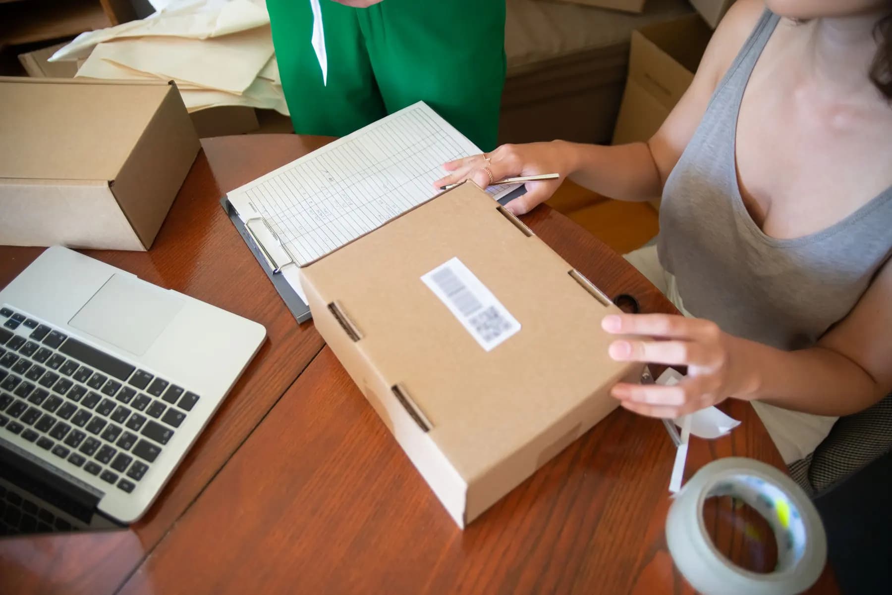 Two people packing online orders by hand next to a laptop