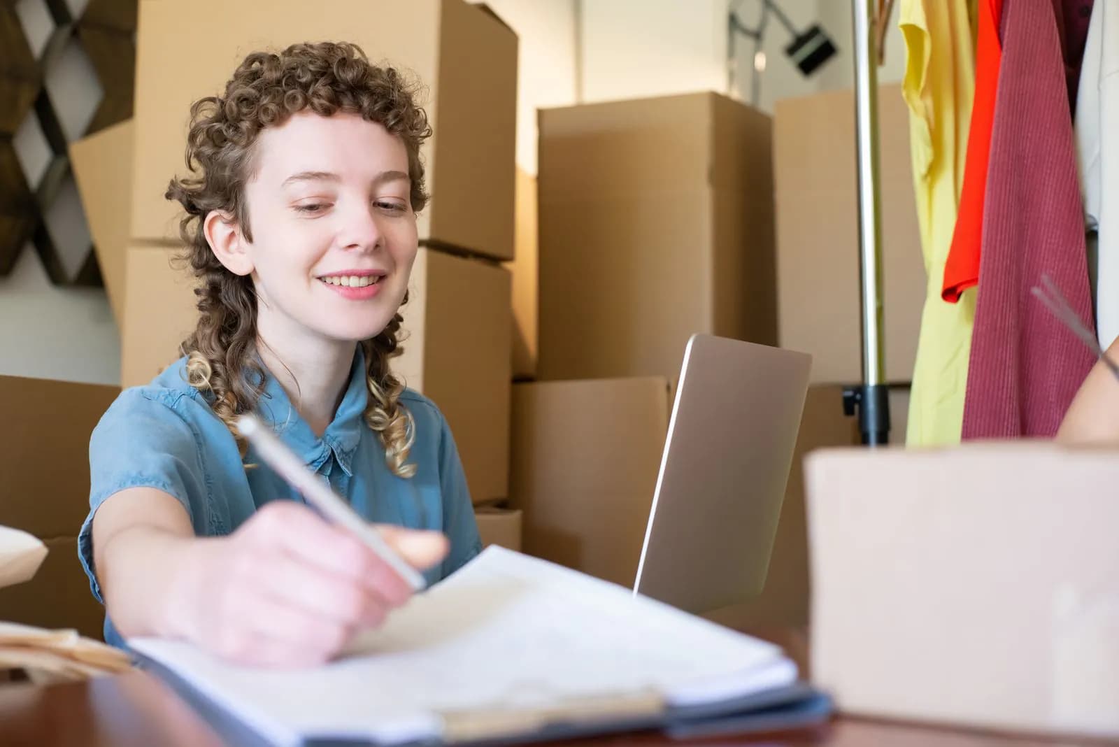A smiling business owner running her shop from a laptop among parcels
