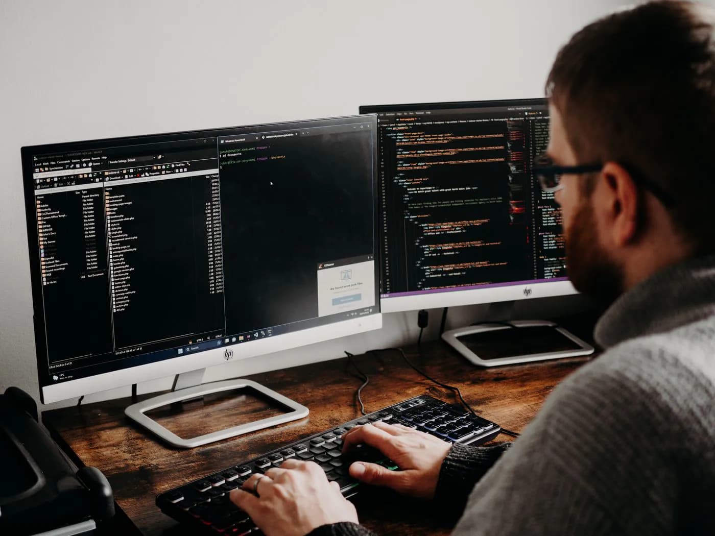 A developer updating code across two monitors at a wooden desk